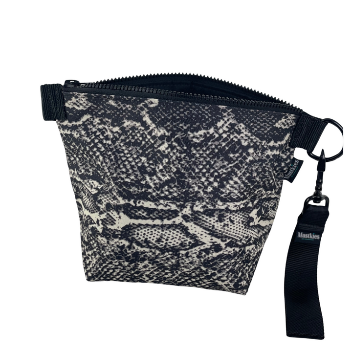 The Voyage clutch from Mustkies, a versatile accessory perfect for both cosmetic storage and everyday use as a daytime carry clutch. Handmade in a waterproof canvas inside and out. Print is a black snake design with black wristlet straps.