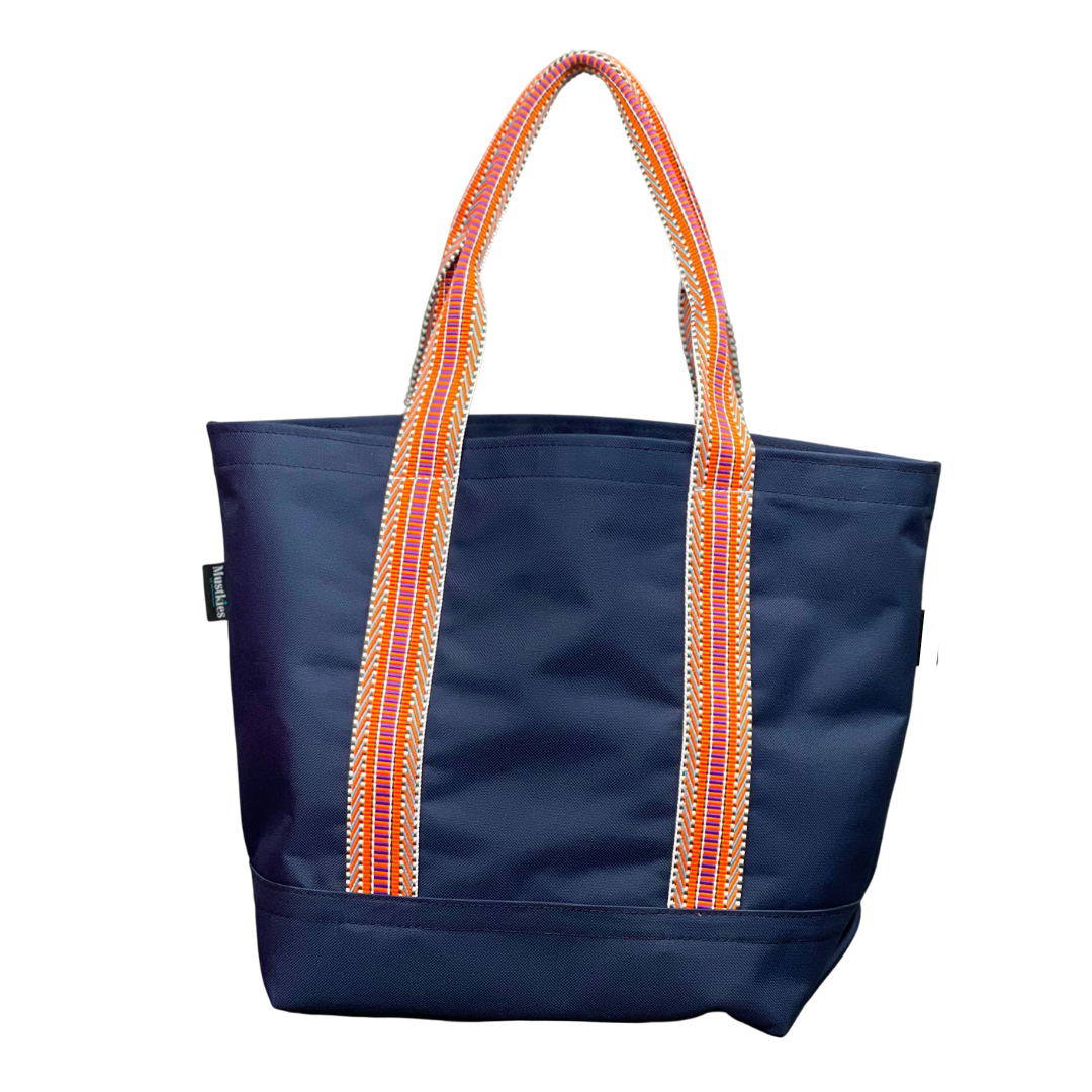 Mustkies Navy Waterproof Canvas Milou Shopper Tote with Orange MultiWebbing. Ultimate Everyday Shopping Tote Bag. Perfect for running errands. Handcrafted with Waterproof Oxford Canvas, which makes it very easy to clean and finished with a Nylon Rainbow Strap. Available in 6 color options. Finished size 10"L x 8"W x 12"T