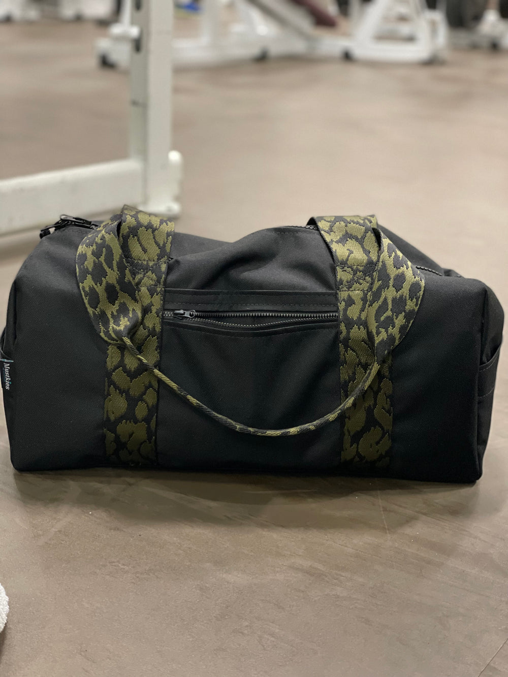 Mustkies Paris Duffel Bag, handmade in a black waterproof canvas and finished in a green camouflage strap. Green lining with 4 exterior and interior pockets. 